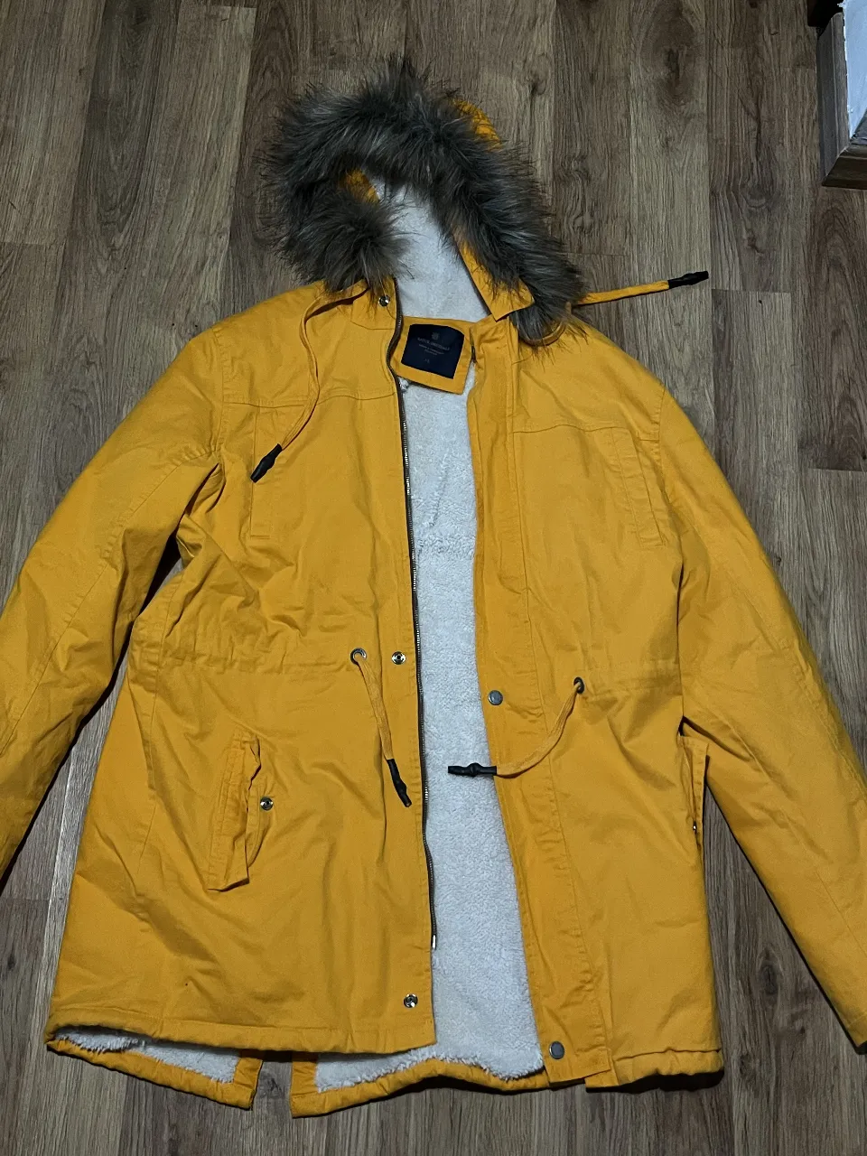 Campera impermeable de color amarillo vibrante, ideal para protegerte del frío y la humedad. Posee un forro interno de corderito súper abrigado y un detalle de piel sintética en la capucha que le da un toque canchero. La piel sintética se puede sacar de la capucha gracias a los botones. Perfecta para un look urbano y moderno.