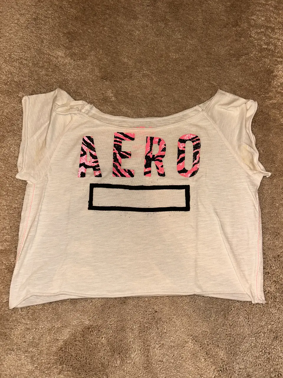 Remera crop de mujer, blanca con estampado "AERO" en rosa y negro con diseño de cebra.  Ideal para un look casual y moderno.