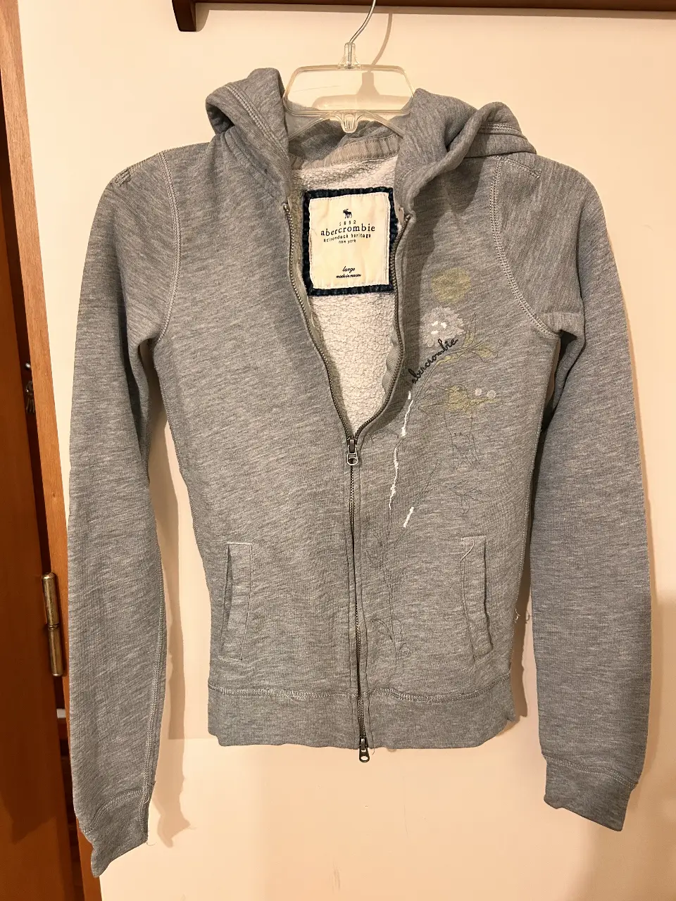 Buzo con cierre gris de la marca Abercrombie Kids, con capucha y detalles bordados. Talle Large.