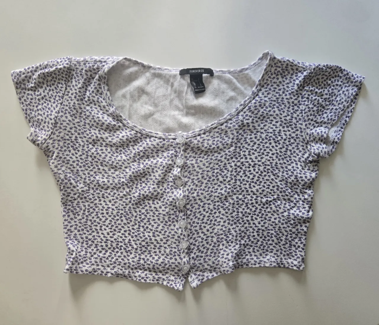 Remera manga corta estampada con flores pequeñas en color violeta. Posee botones en la parte delantera.