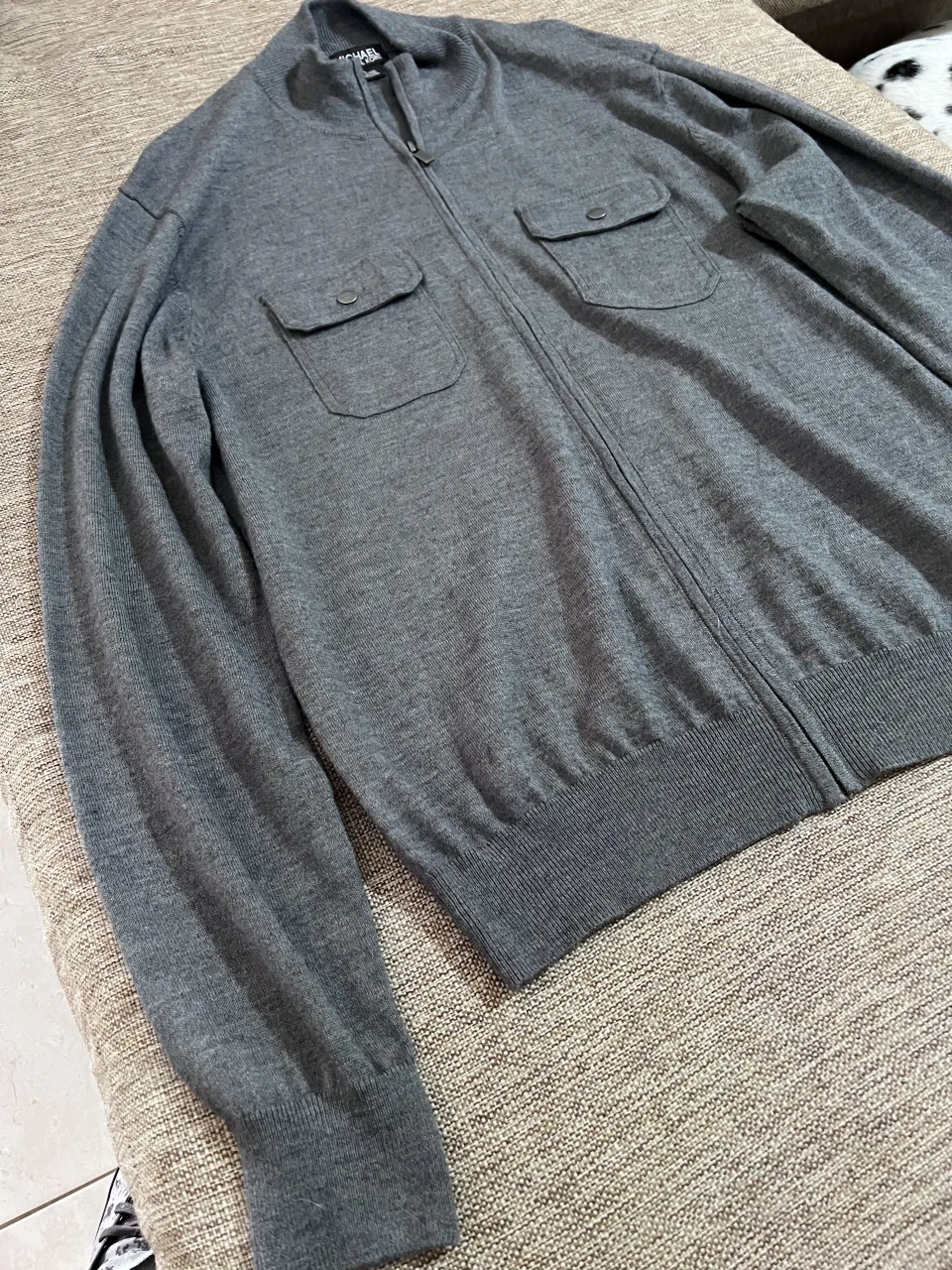 Sweater gris con cierre completo y cuello mao. Posee dos bolsillos superiores con tapa y botón.