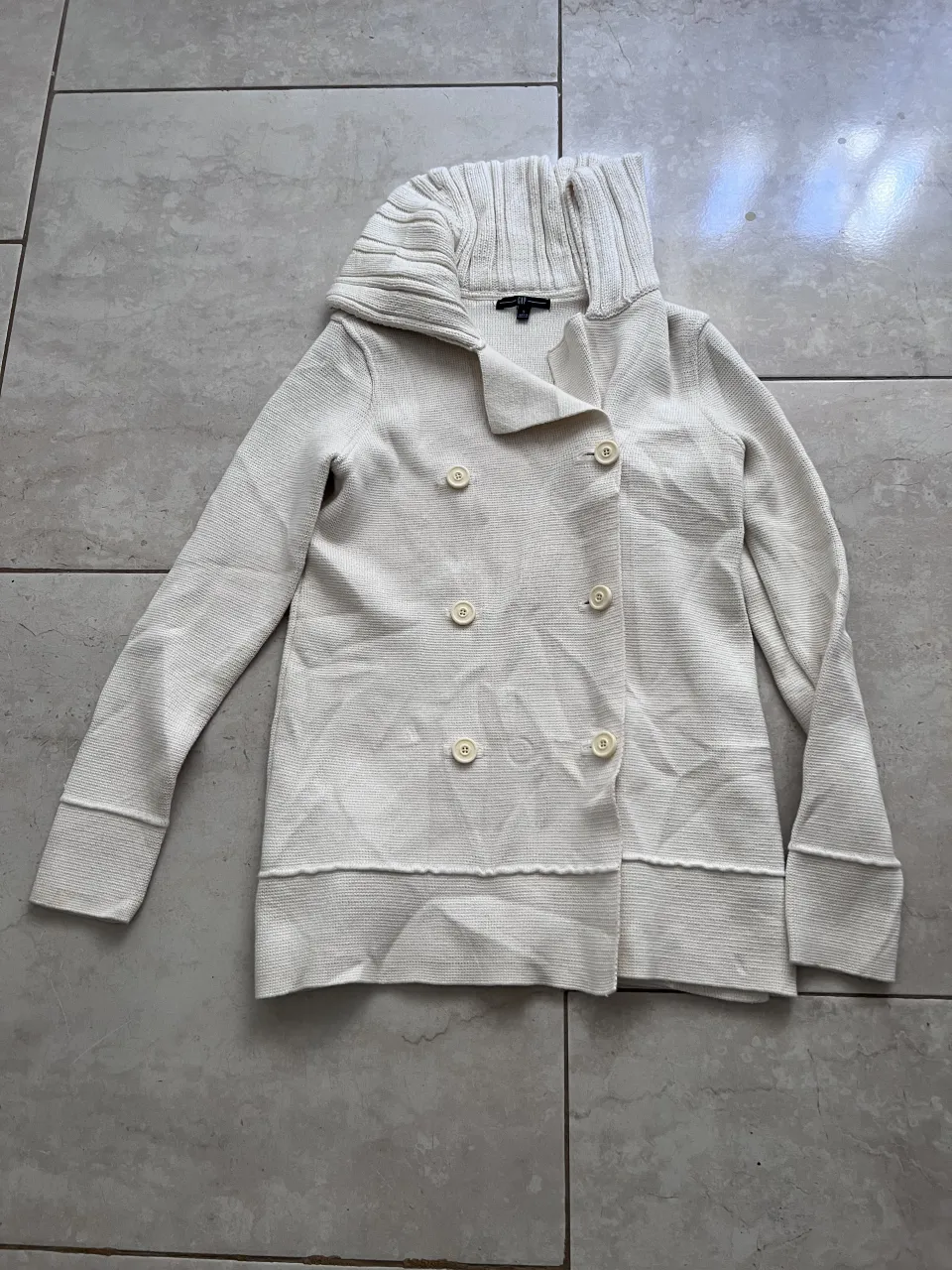 Cardigan de tejido de punto color crudo con cuello alto y botones al frente. Tiene dos filas de botones y puños tejidos.