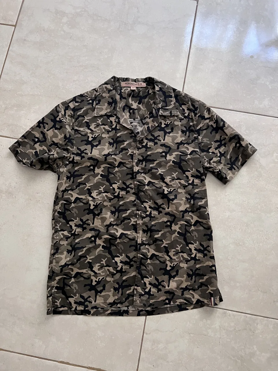 Camisa de manga corta con estampado de camuflaje. Cuello camisero y botones al frente.