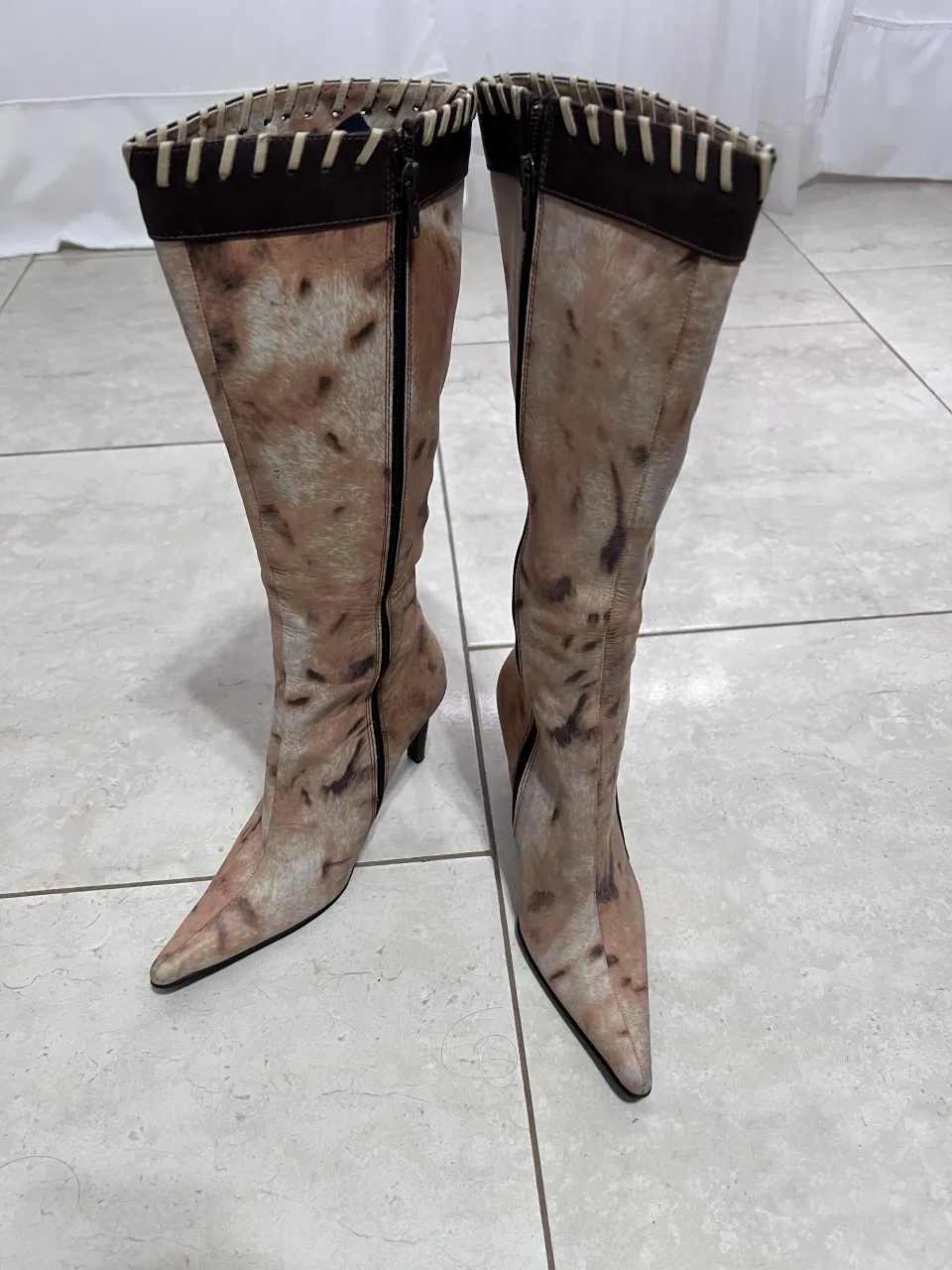 Botas de caña alta con estampado animal print en tonos beige y marrón. Cierre lateral y detalle de costuras en la parte superior y lateral. Taco fino.