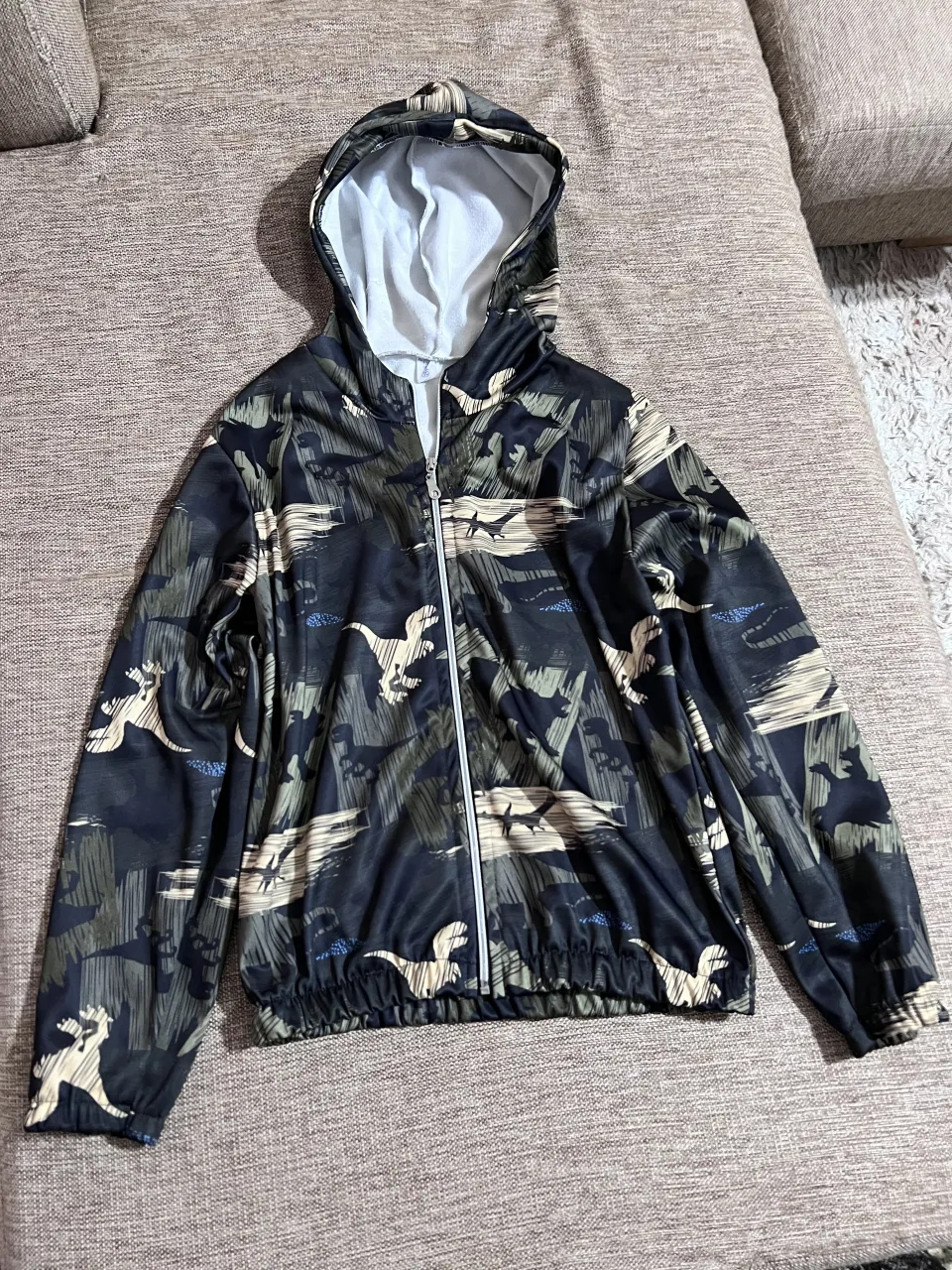 Campera con capucha y cierre completo. Estampado de camuflaje con dinosaurios.