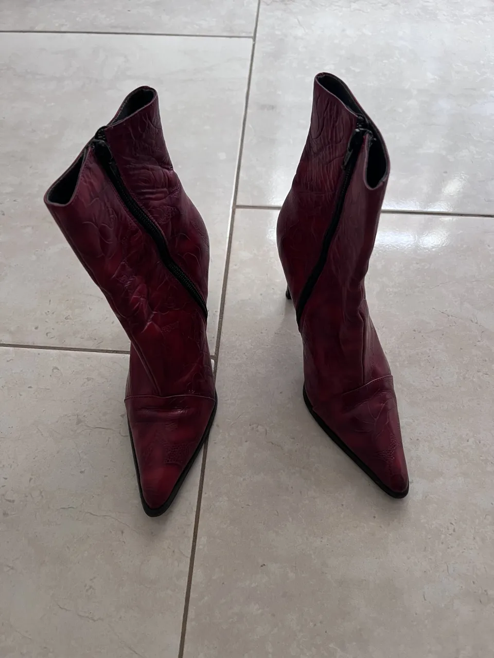 Botitas de cuero color bordó con cierre lateral y taco alto. Tienen un diseño grabado en toda la superficie.