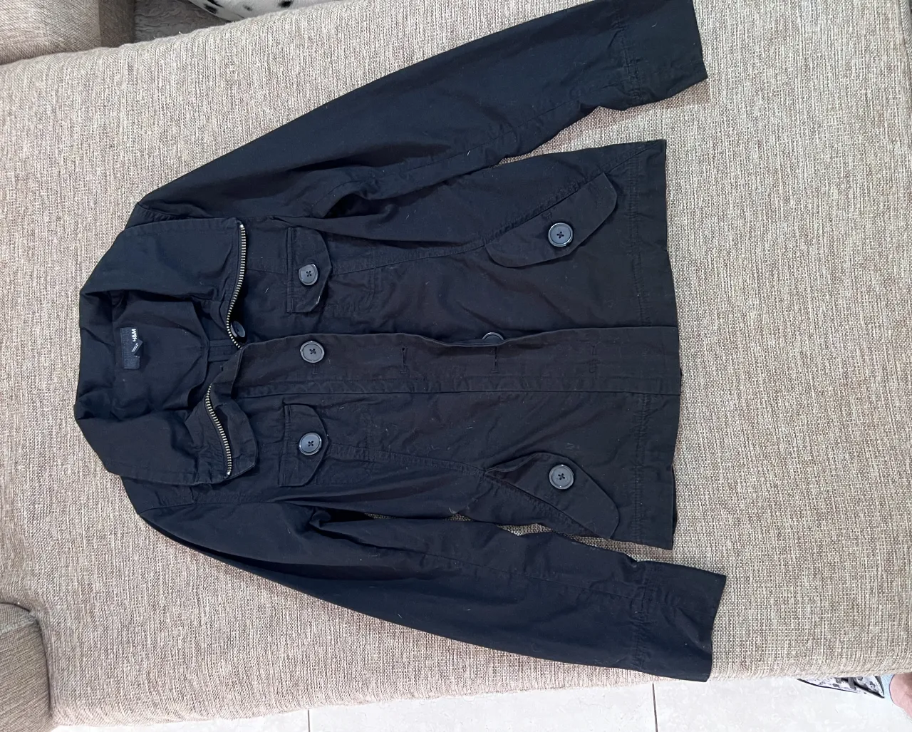 Campera negra con cuello, cierre y botones al frente. Posee bolsillos con solapa y botón en el frente.