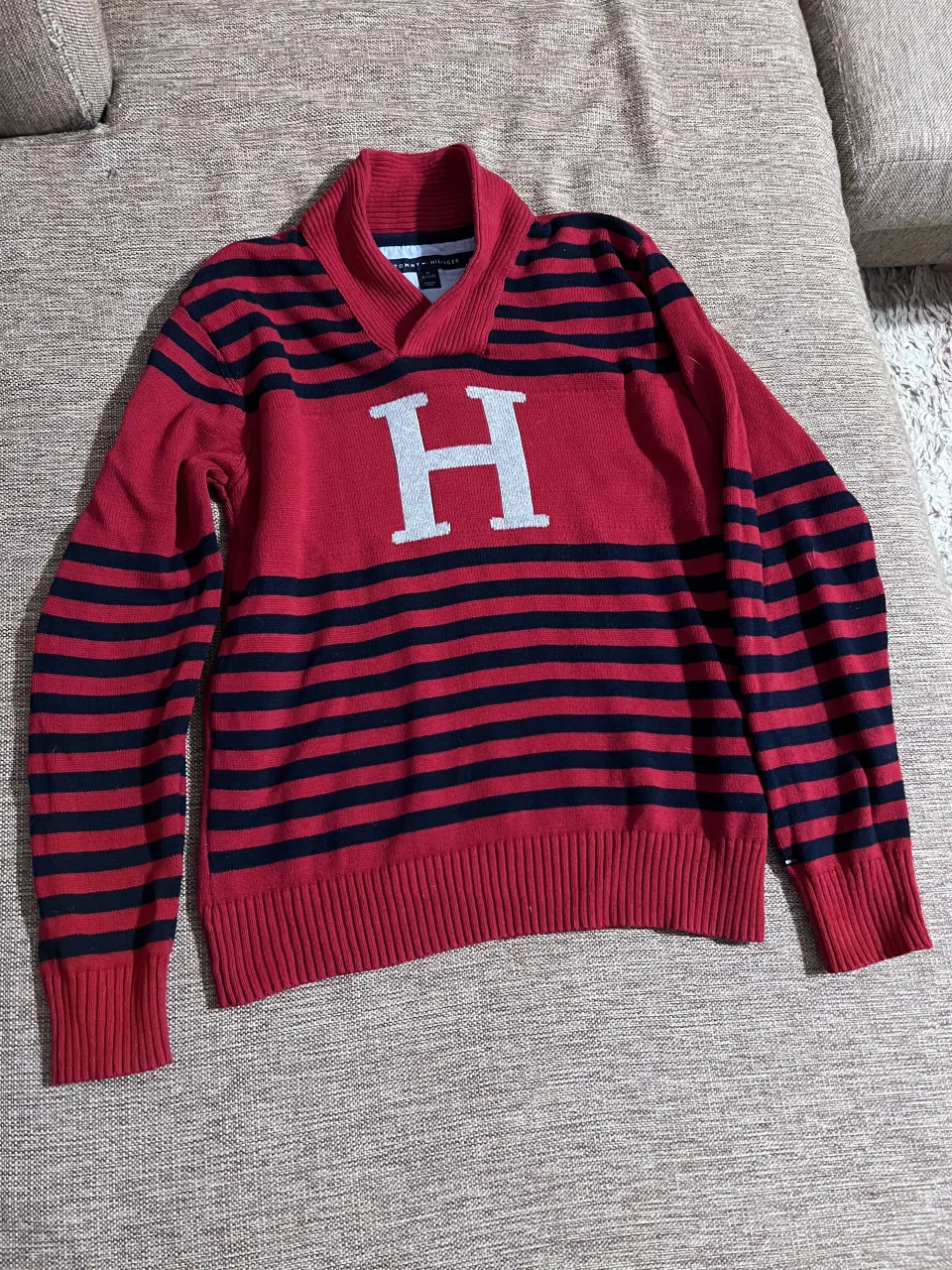 Sweater de algodón a rayas rojas y azul marino. Posee un cuello tipo V con solapas y la letra "H" estampada en blanco en el frente.