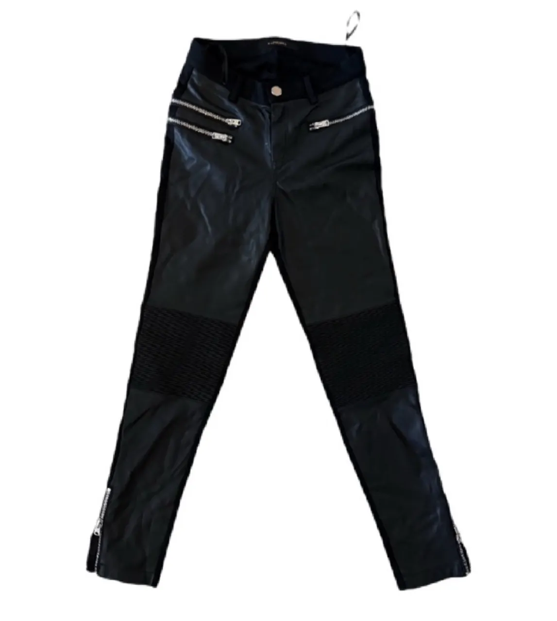 Pantalón de cuero sintético negro, tiro alto, con detalles de cierres plateados en los bolsillos y en los tobillos. Diseño tipo biker con costuras acolchadas en las rodillas. Ideal para un look rocker o edgy.