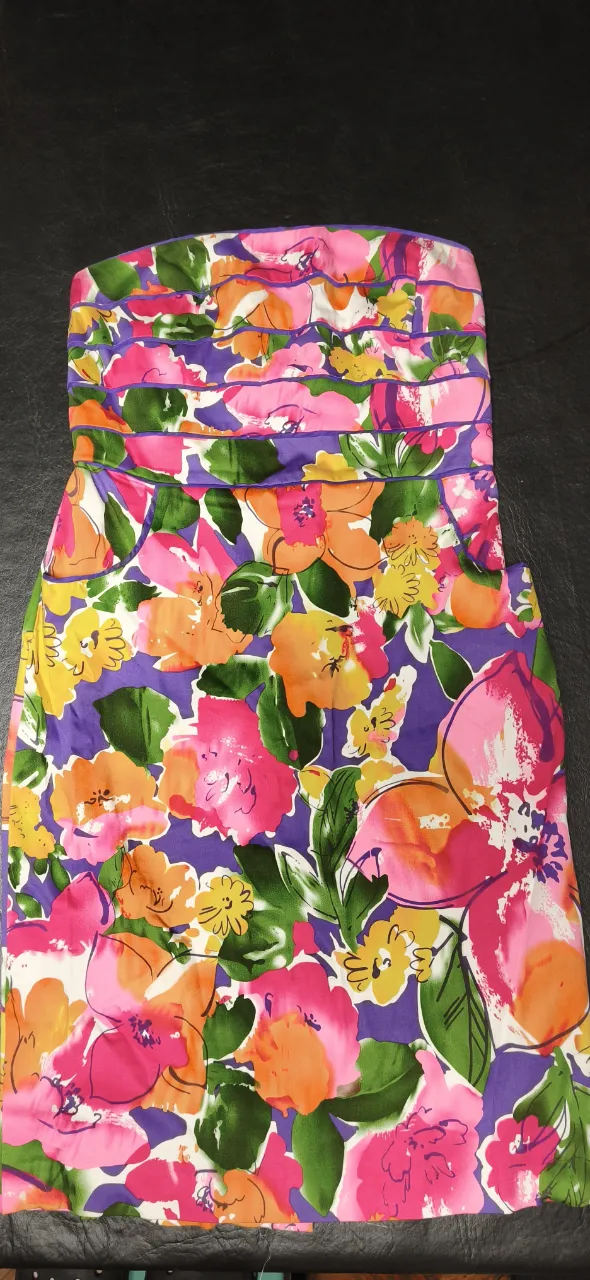 Vestido strapless con estampado floral vibrante en tonos fucsia, naranja, amarillo, verde y violeta. Posee fruncido en la parte superior del busto y cierre metálico en la espalda. Con varillas en el busto.