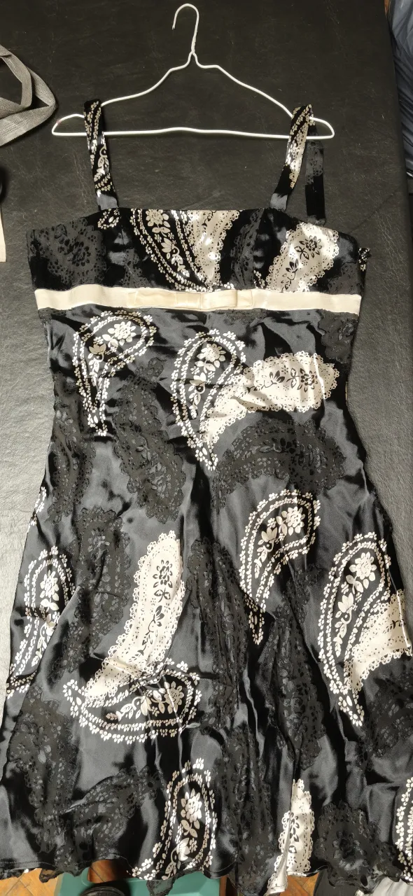 Vestido negro con estampado de paisley en blanco y detalles en negro. Posee tirantes finos y un detalle de cinta blanca en la cintura. 