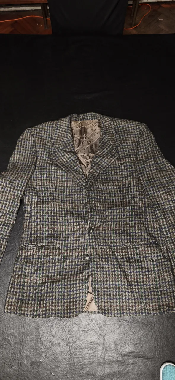 Blazer de paño a cuadros en tonos verdes, marrones y azules. Posee dos botones en la parte frontal y bolsillos con solapa. El interior es de saten color beige.