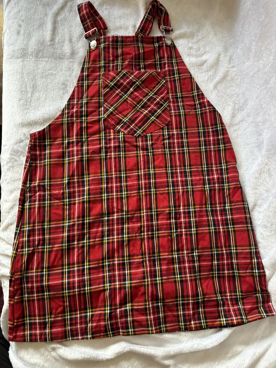 Vestido jardinero de mujer, con estampado a cuadros en tonos rojos y negros. Ideal para un look casual y moderno. Cuenta con tirantes ajustables y un bolsillo frontal.