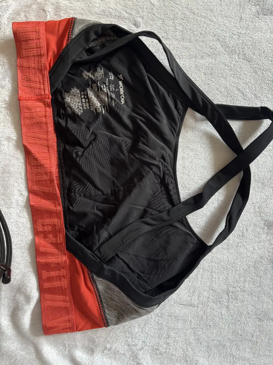 Top deportivo para mujer, negro con detalles en gris y naranja. Ideal para actividades de alto impacto. Marca WORKOUT.