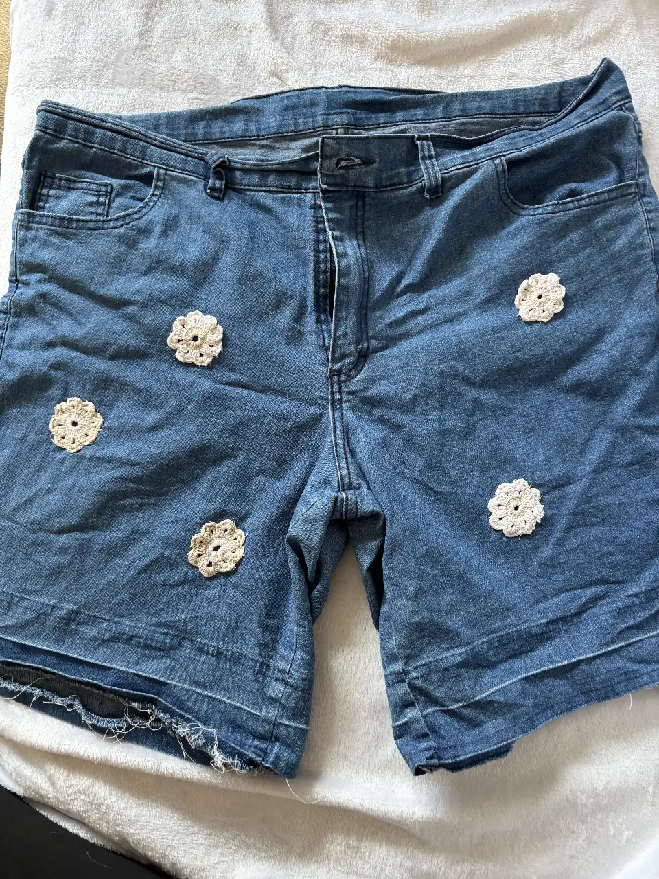 Short de jean azul con detalles artesanales de flores de crochet color crudo. Ideal para un look casual y fresco.