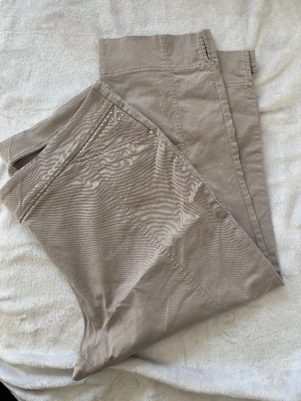 Pantalón capri stretch color gris claro con detalles de strass en los bolsillos delanteros. Tiro medio y corte recto. Ideal para un look casual y súper cómodo.