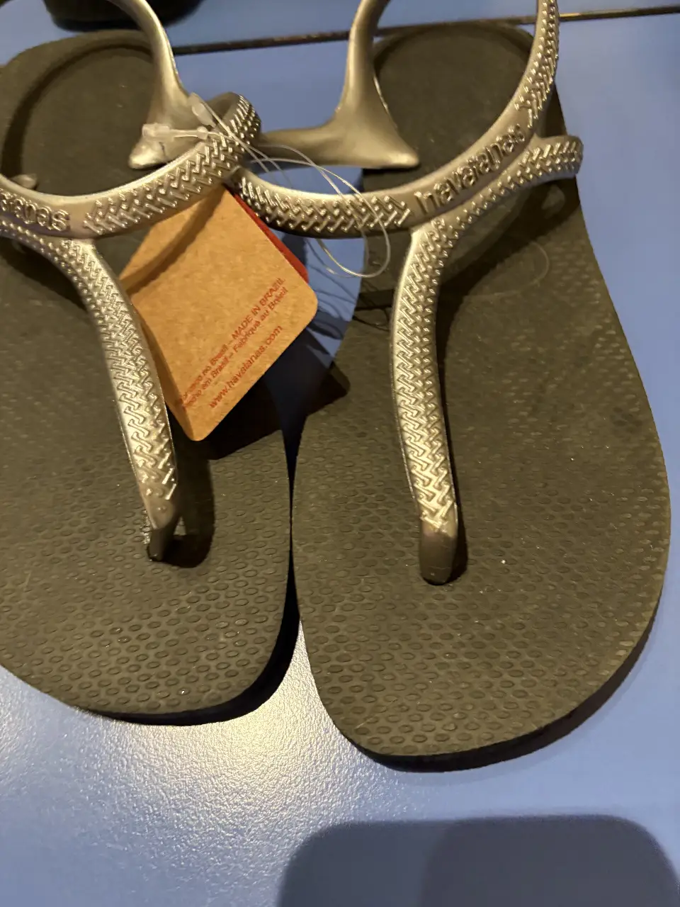 Sandalias Havaianas con tiras plateadas y suela negra. Ideales para el verano y la playa.