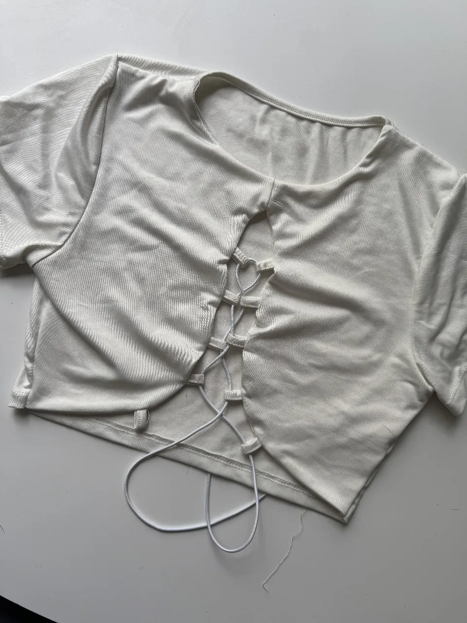 Top blanco escotado con cordones cruzados en el frente. Manga corta y corte al cuerpo