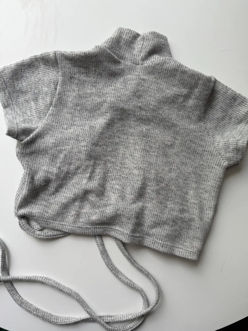Top gris de cuello alto con mangas cortas y detalle de fruncido y lazo en la parte  de atrás. 