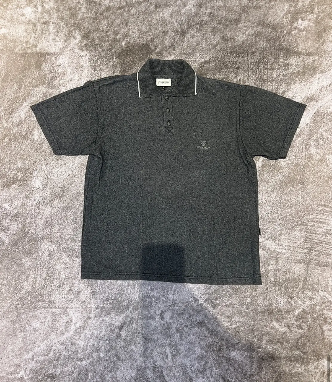 Remera polo gris oscuro de hombre, con cuello y detalles blancos. Tiene el logo de Givenchy bordado en el pecho. Ideal para un look casual y elegante. MEDIDAS: Talle: M/L - Largo: 65 - Ancho: 58