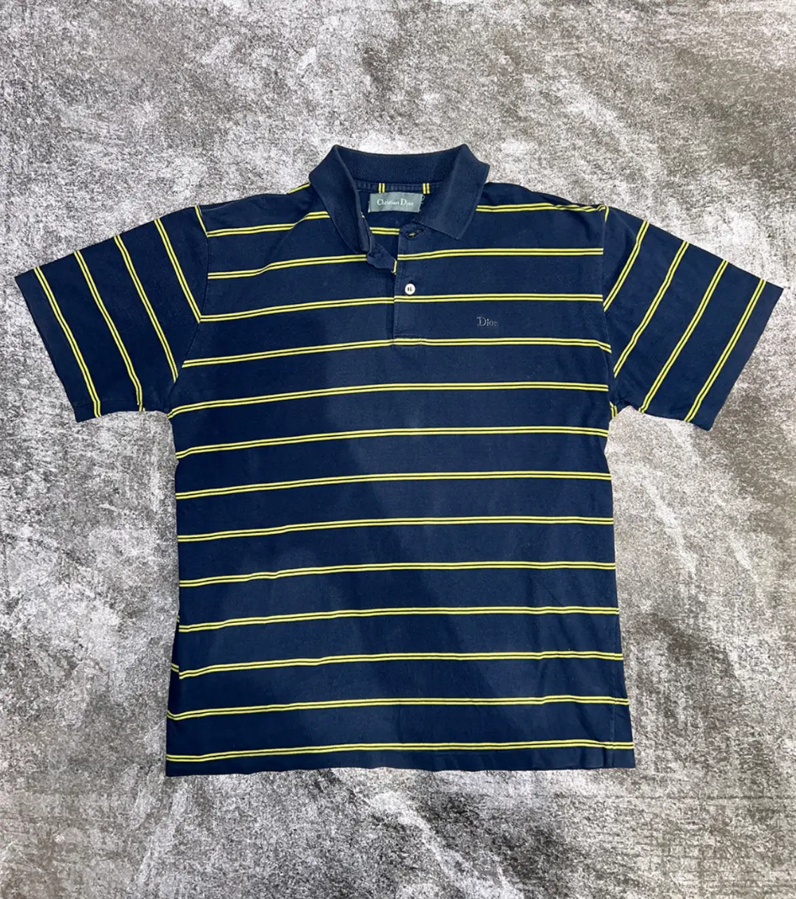 Remera polo Christian Dior azul marino con rayas amarillas. Clásico diseño a rayas horizontales, ideal para un look casual y elegante. MEDIDAS: Talle: M - Largo: 62 - Ancho: 55