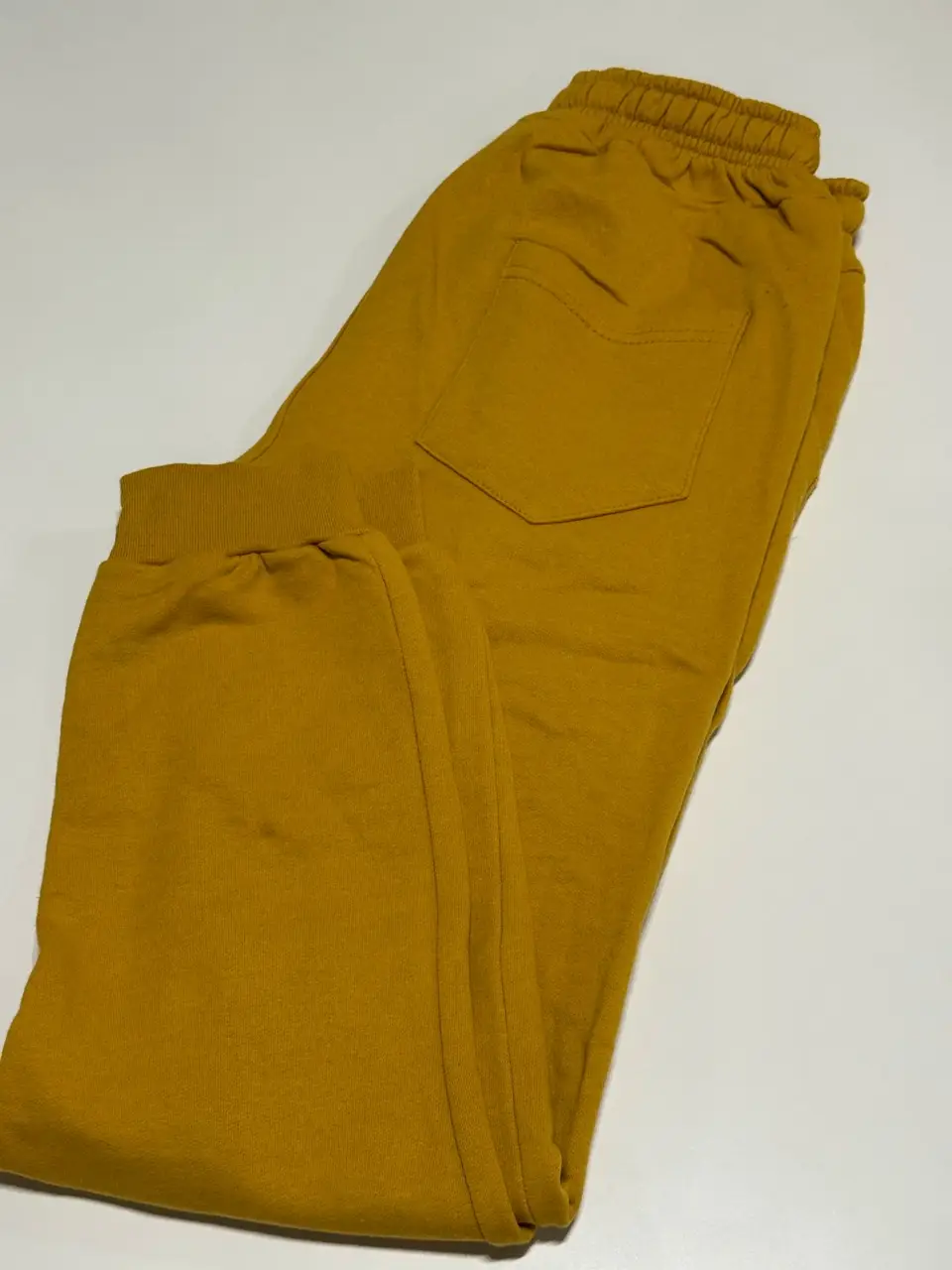 Pantalón de jogging de algodón color mostaza, con bolsillo trasero y puños en los tobillos. Talle M/2. Cintura: 64 cm, estirada hasta 100 cm. Largo: 92 cm.