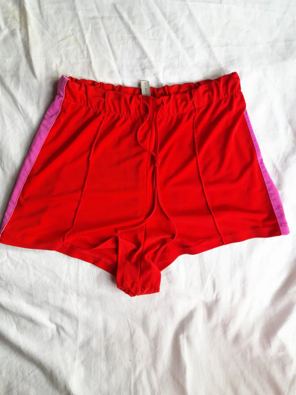 Shorts de color rojo con detalles laterales en color rosa. Cintura elastizada con cordón.