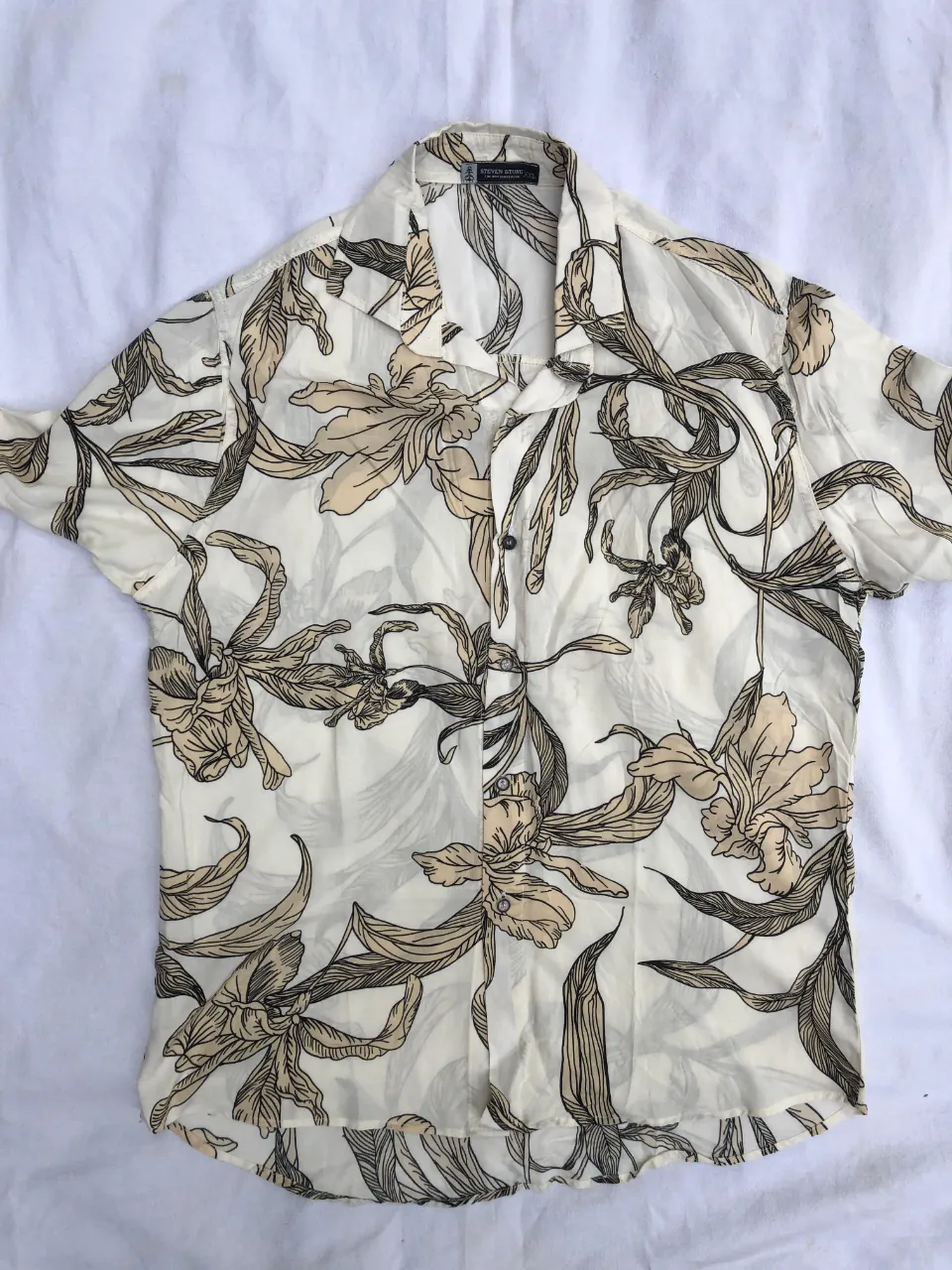 Camisa estampada con flores y hojas en tonos blanco, beige y negro. Manga corta y cuello clásico.
Medidas:
hombros 48cm
axilas 60cm 