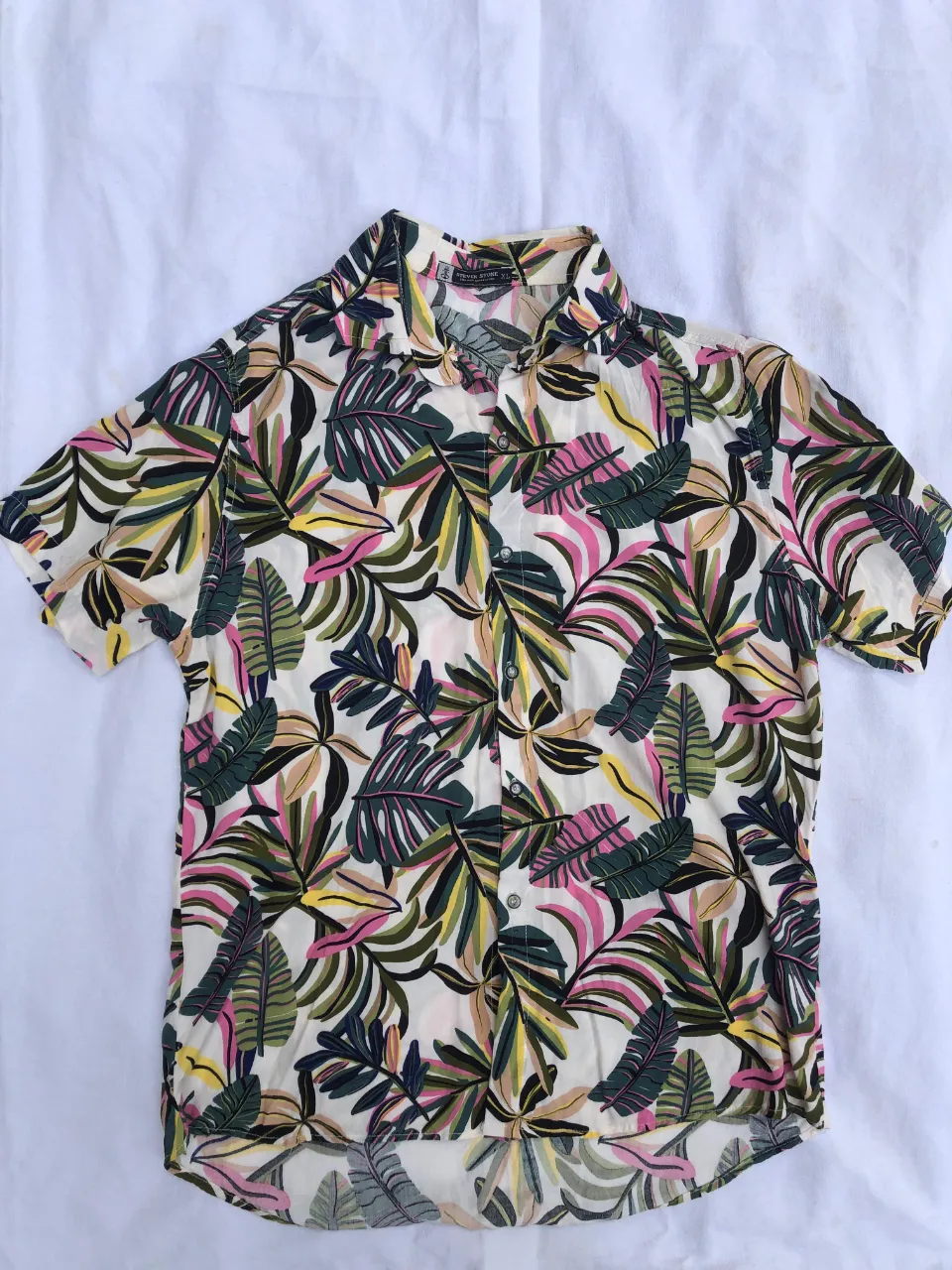 Camisa de manga corta con estampado de hojas tropicales en blanco, verde, rosa y amarillo. Cuello camisero y botones al frente. 
Medidas:
hombros 46cm 
axilas 58cm
