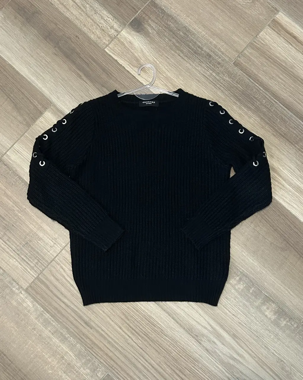 Sweater negro de punto con detalles de ojales metálicos en las mangas. Ideal para un look casual y moderno.