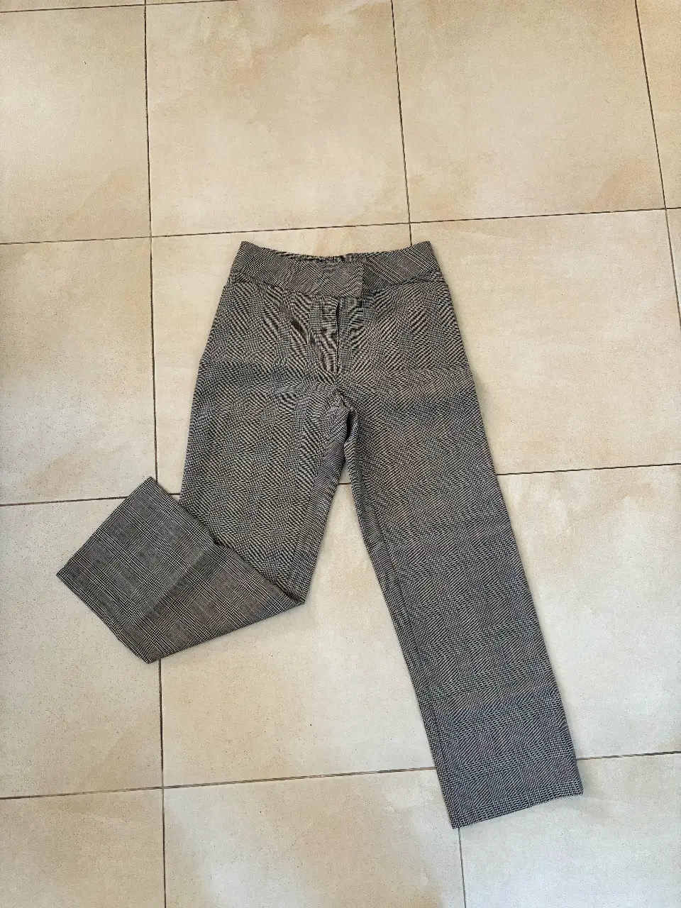 Pantalón sastrero de mujer, con estampado a cuadros en tonos grises y blancos. Corte recto y elegante, ideal para un look formal o de trabajo.