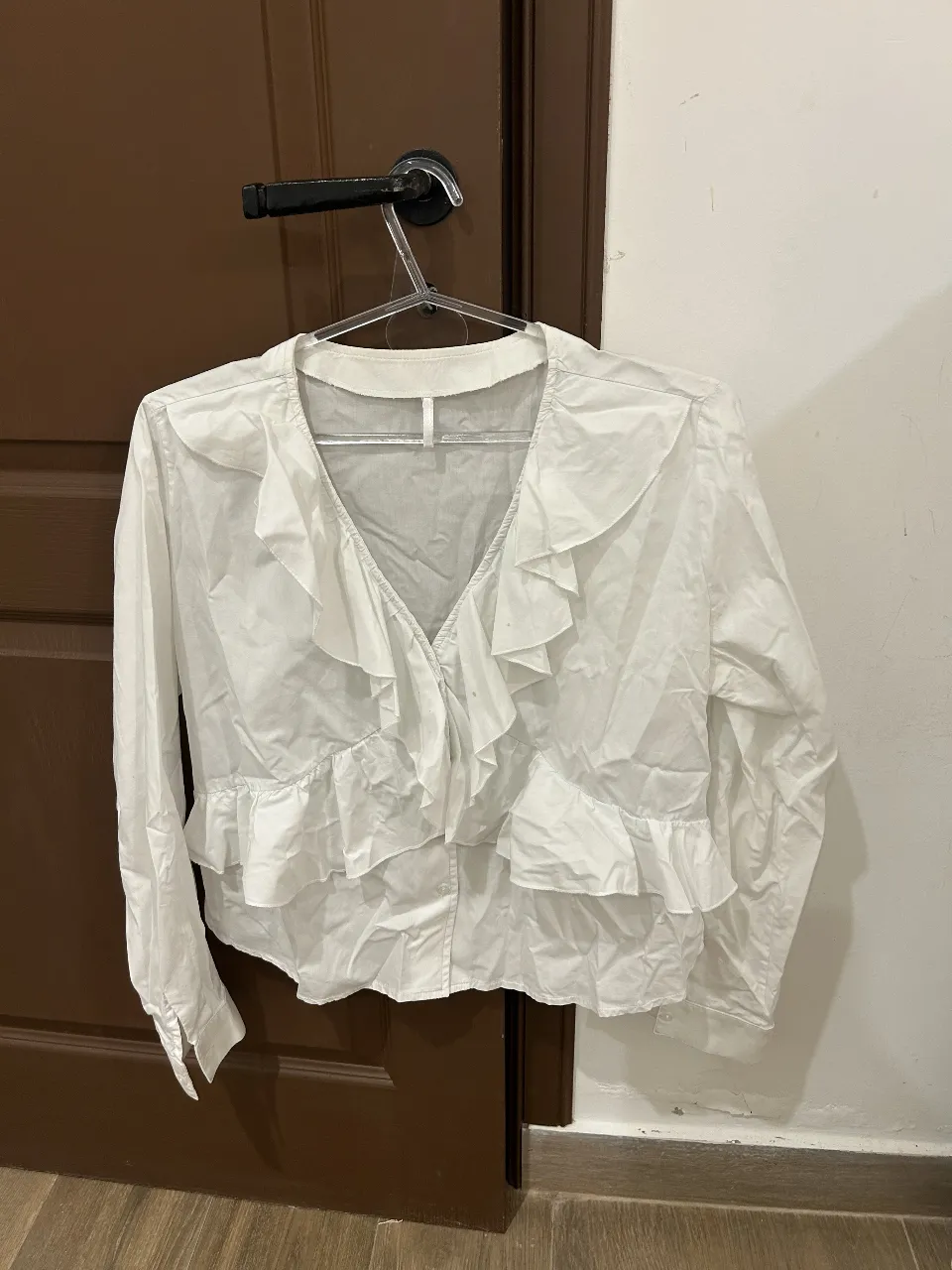 Blusa blanca con volados y escote en V. Manga larga con puño. Perfecta para un look elegante y femenino.