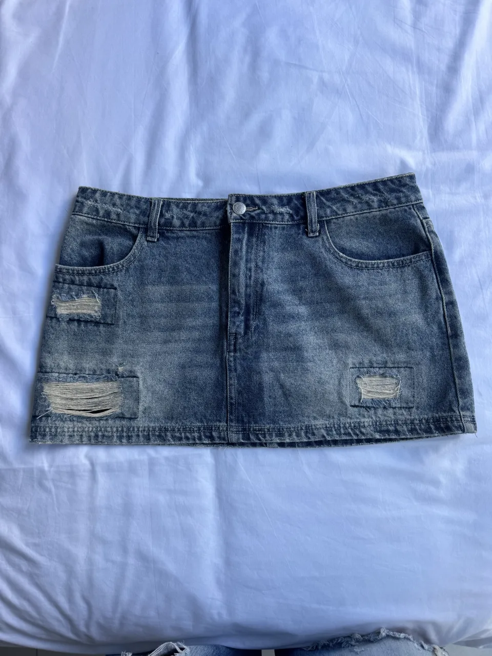 Pollera de jean corta con roturas y desgastes. Tiene bolsillos delanteros y traseros.