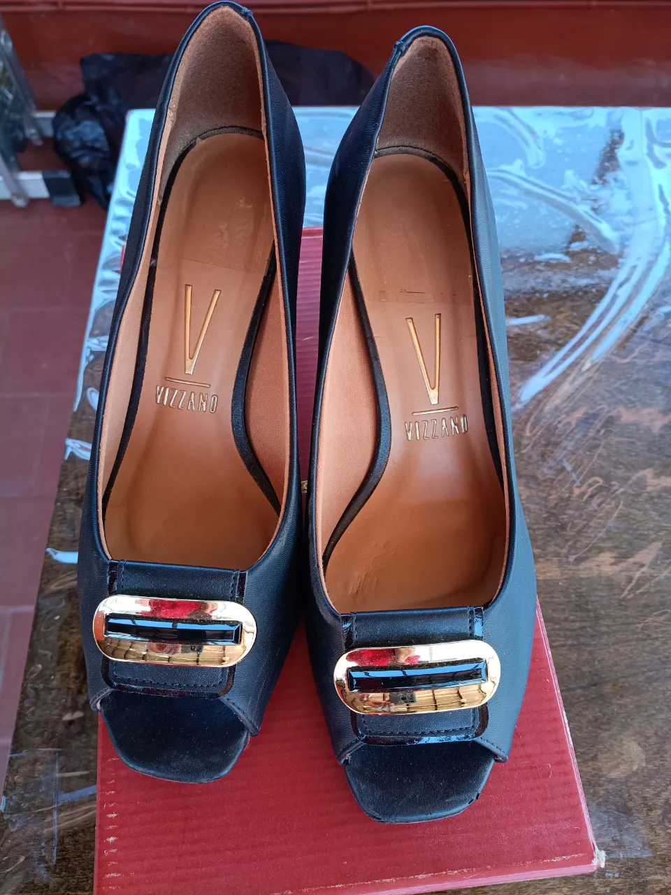 Zapatos de taco alto negros, con puntera abierta y detalle de hebilla dorada con piedra negra en la capellada. Marca Vizzano.