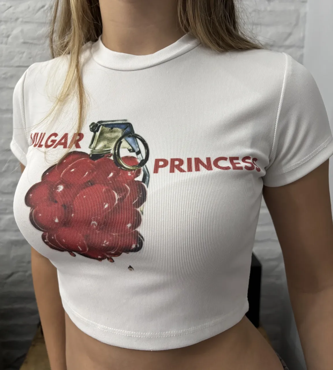 Remera blanca manga corta y corte crop. Estampa frontal de una granada roja con la inscripción "VULGAR PRINCESS" en letras rojas.