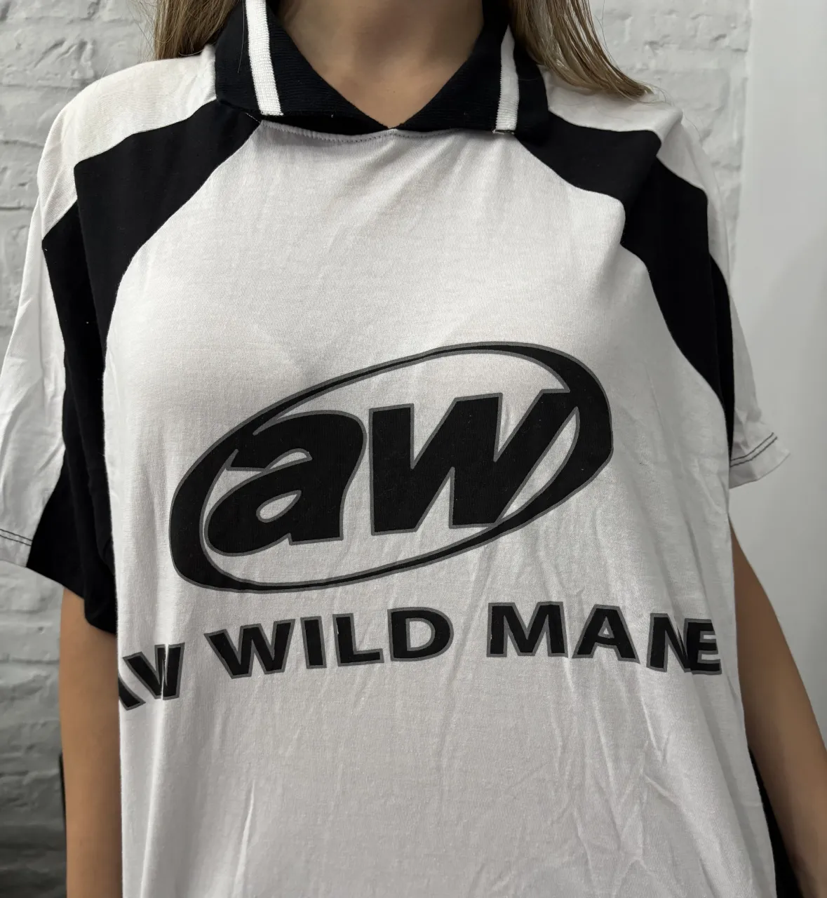 Remera blanca con mangas cortas y cuello polo. Presenta estampa grande en el frente con el logo 'aw'.  Las mangas y los laterales son de color negro. Sin uso,  M/L