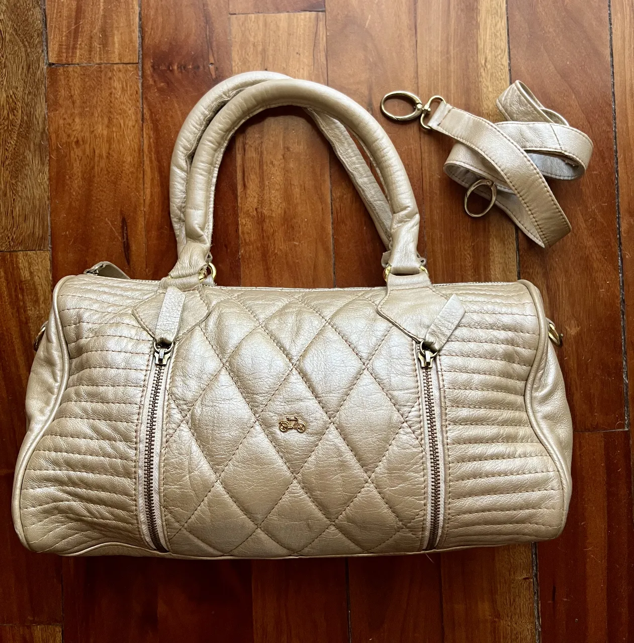 Bolso Satori crudo perlado, estilo baúl, con costuras en rombos y detalles dorados. Incluye correa para colgar.