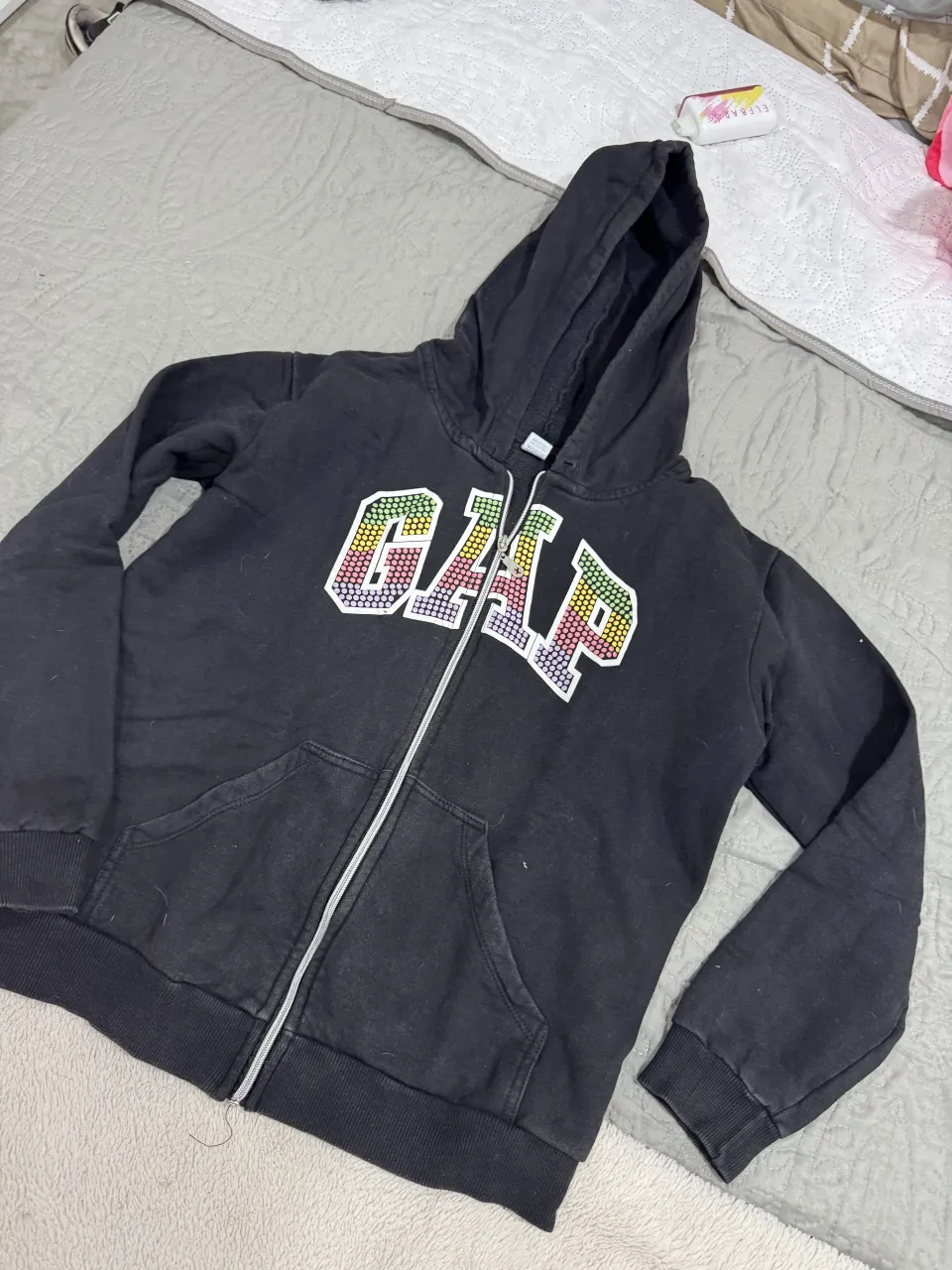 Buzo negro con capucha y cierre completo. Presenta el logo de la marca en el frente con letras de colores y detalles brillantes.