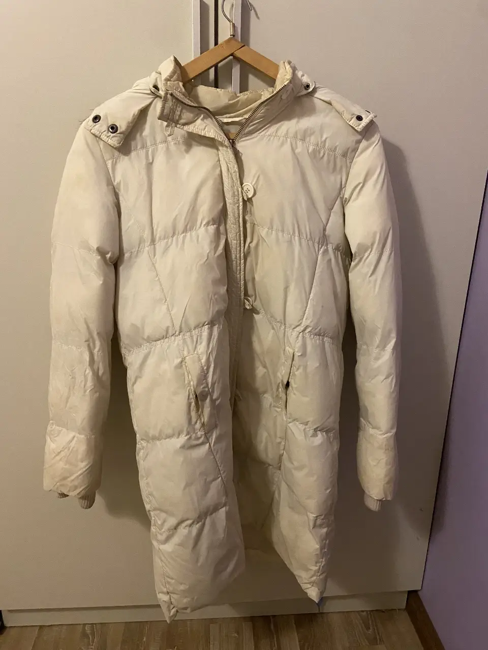Campera larga de pluma para mujer, color blanco. Ideal para el invierno, con capucha y detalles de piel en el borde. Posee cierre y bolsillos.
