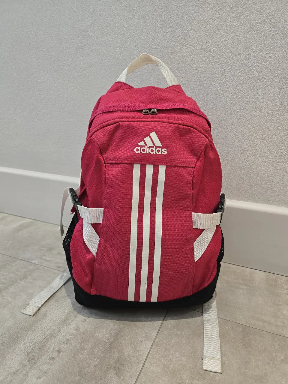 Mochila rosa mediana de la marca Adidas, ideal para el día a día o para llevar tus cosas al gimnasio. Cuenta con el logo y las tres tiras clásicas de la marca en blanco. Tiene bolsillos laterales de red y correas ajustables para mayor comodidad. Tiene unos detalles que se pueden ver en las últimas 2 fotos. Medidas 
alto: 38cm. 
ancho (base): 14cm. 