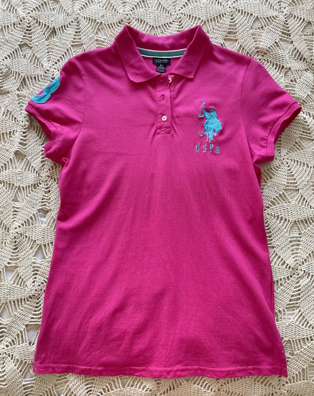 Remera polo de mujer, color fucsia con logo de la marca US Polo Assn. en celeste en el pecho y en la manga. Ideal para un look casual y deportivo.
talle dice xl pero sería más para un M,L