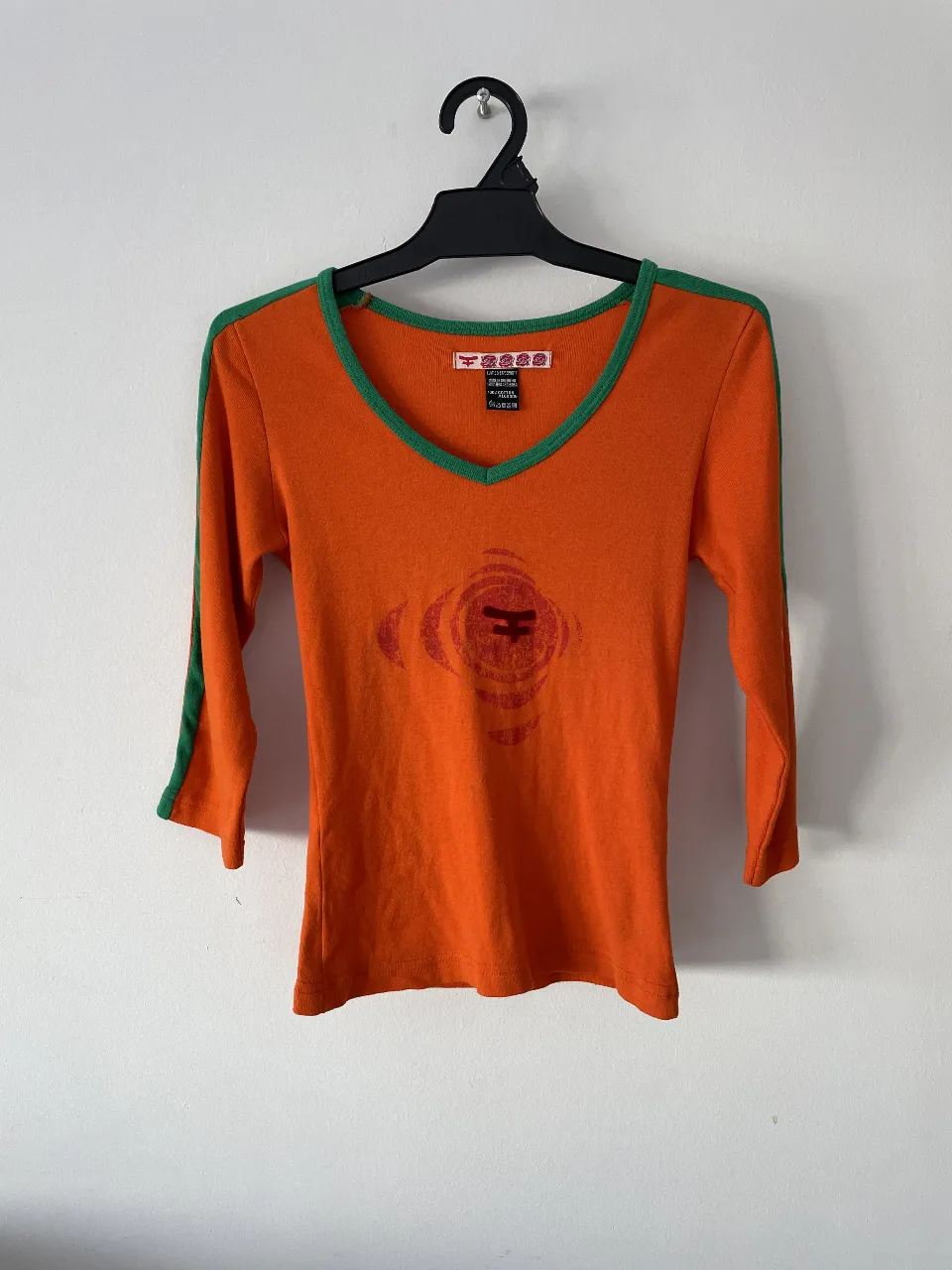 Remera manga 3/4 naranja con detalles verdes en cuello y mangas. Estampado en el frente. Ideal para un look casual y con onda.