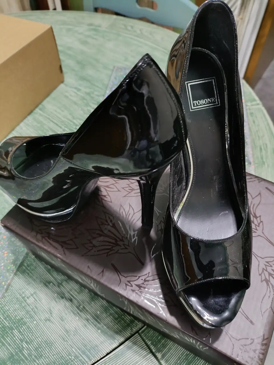Elegantes zapatos de tacón alto negros de charol, ideales para fiestas y eventos formales. Diseño clásico con punta abierta y detalles plateados.