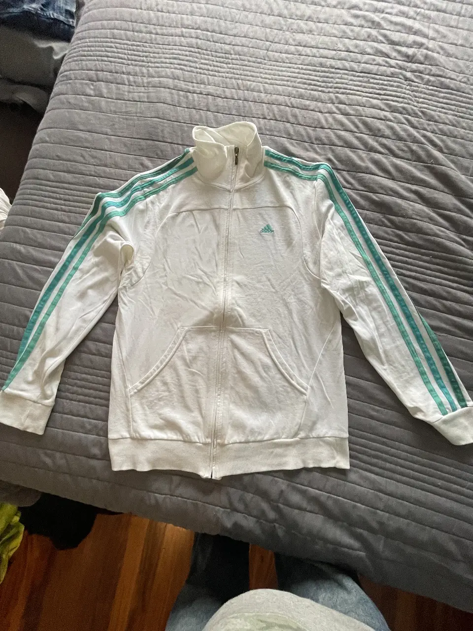 Buzo Adidas blanco con cierre y detalles en verde. Ideal para un look deportivo y casual.
