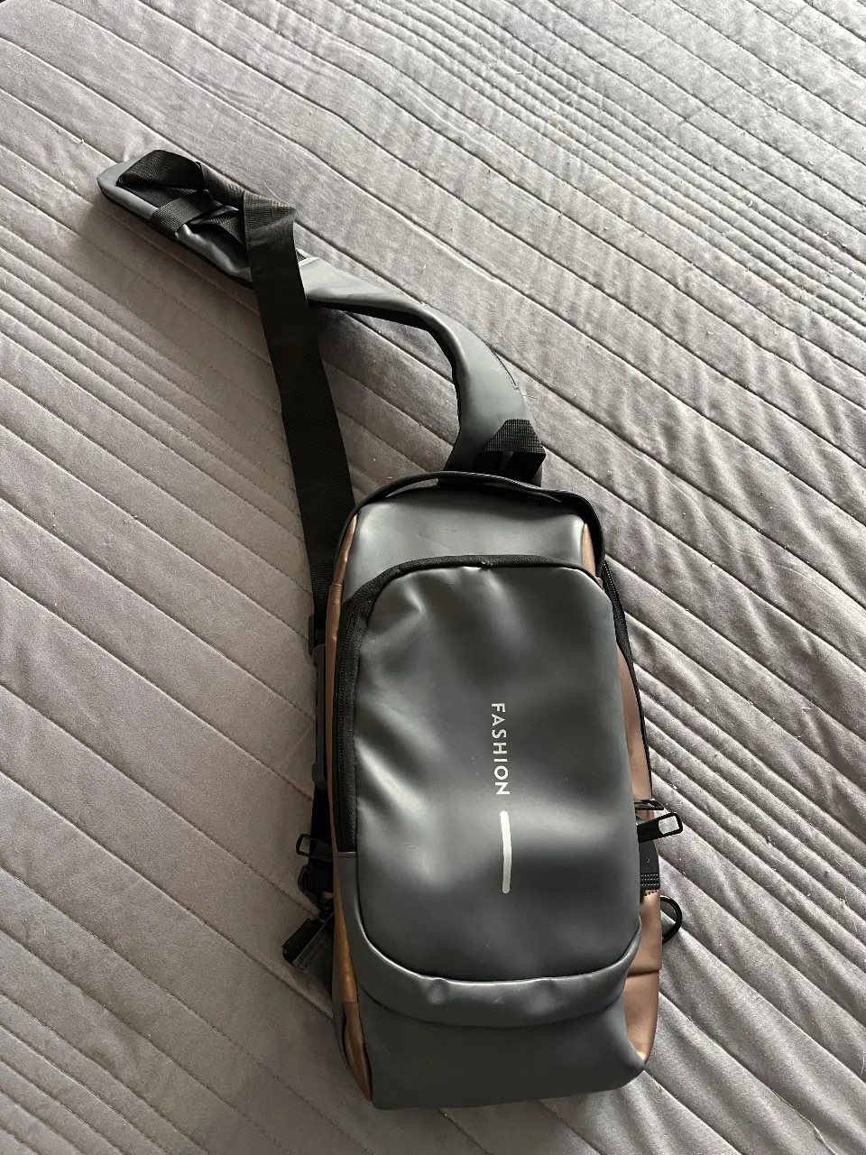 Bandolera para hombre, color gris con detalles dorados. Ideal para llevar lo esencial con estilo y comodidad. Diseño moderno y funcional.