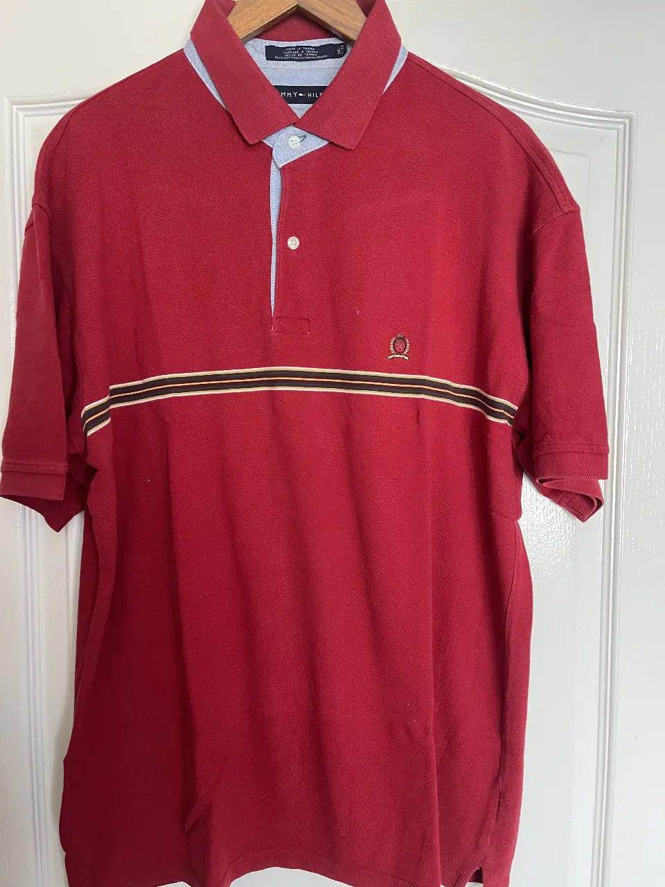 Remera polo roja de hombre, con detalles en amarillo y negro. Cuello y terminación de mangas en azul claro. Logo bordado en el pecho. Ideal para un look casual y cómodo.