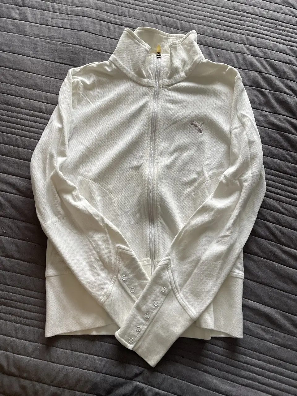 Buzo deportivo blanco con cierre y logo Puma. Ideal para actividades físicas o uso casual.
