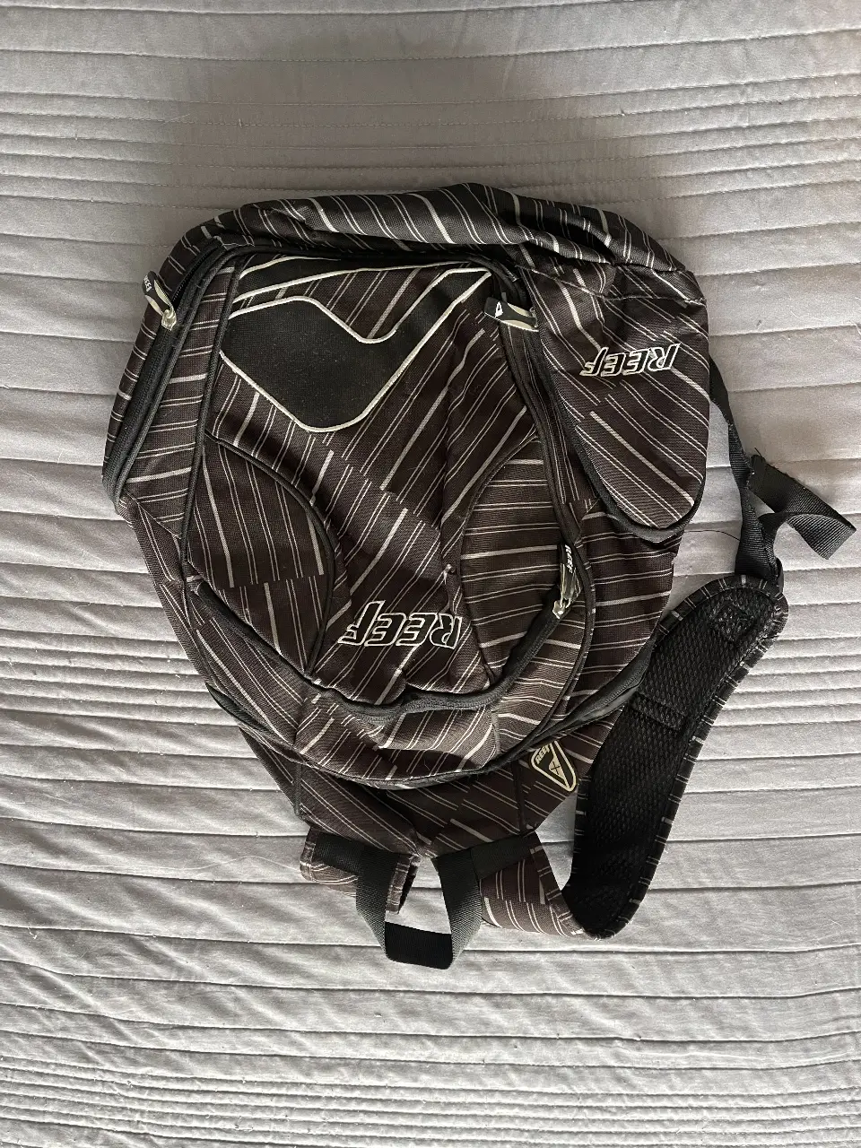 Mochila Reef con diseño a rayas en tonos negro y blanco. Ideal para llevar tus cosas con estilo y comodidad.