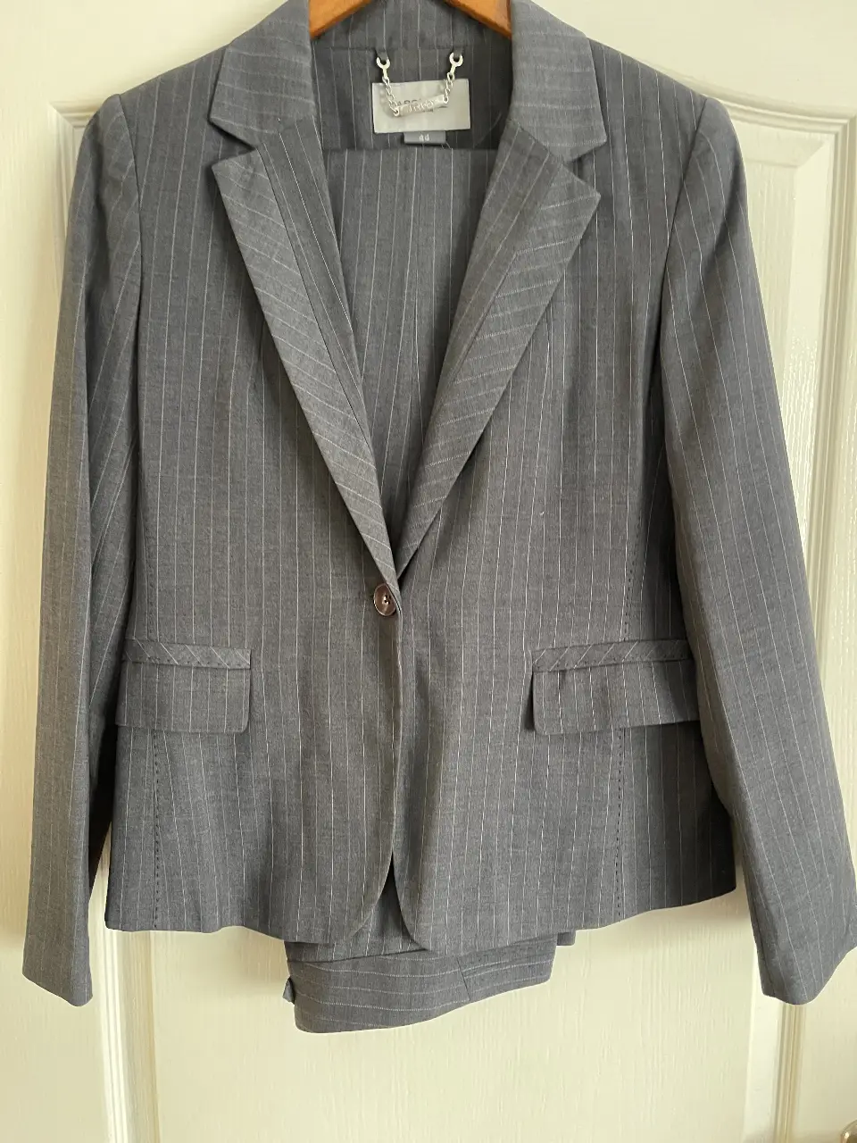 Traje sastrero de mujer, color gris con finas rayas verticales. Incluye blazer con un botón y dos bolsillos delanteros, y pantalón de corte recto con bolsillos.