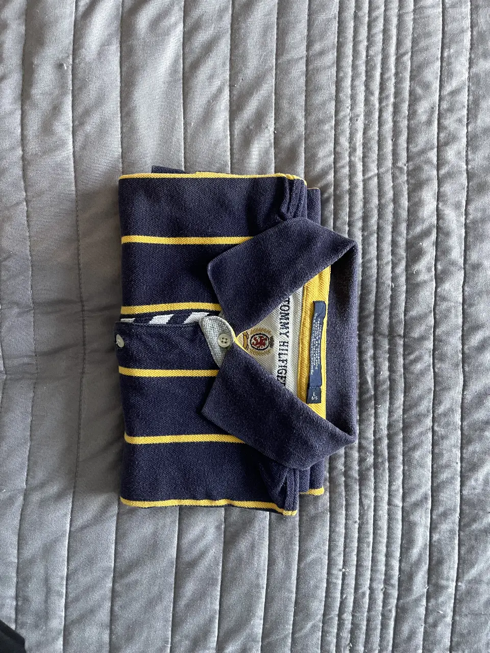 Remera polo Tommy Hilfiger a rayas verticales amarillas y azul marino. Cuello y mangas con detalles en amarillo. Ideal para un look casual y preppy.
